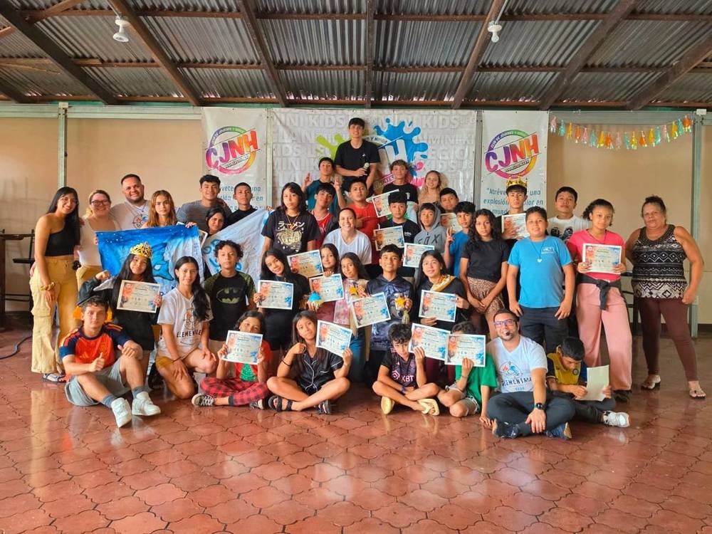 Foto grupal de participantes y personas adultas en un salón; muchos sostienen certificados, frente a rótulos con el logo de la fundación