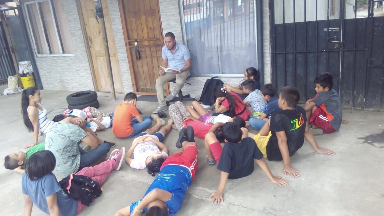 Niñas, niños y jóvenes sentados y acostados en el piso de un corredor, con una persona sentada al fondo