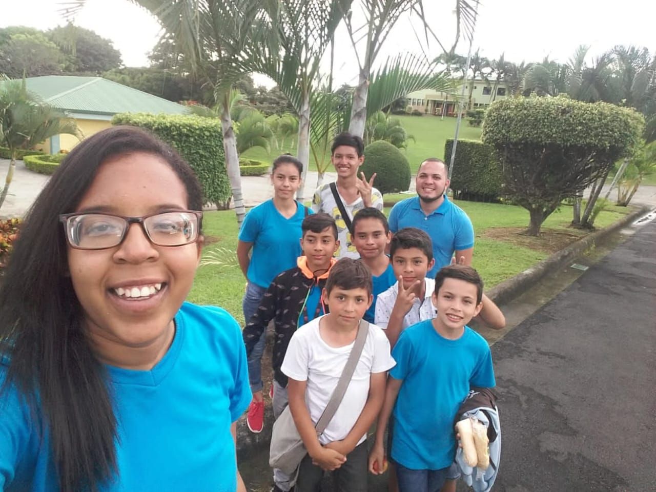 Una joven sonriente se toma una selfi junto a un grupo de niños y adolescentes con camisetas azul turquesa, en un jardín