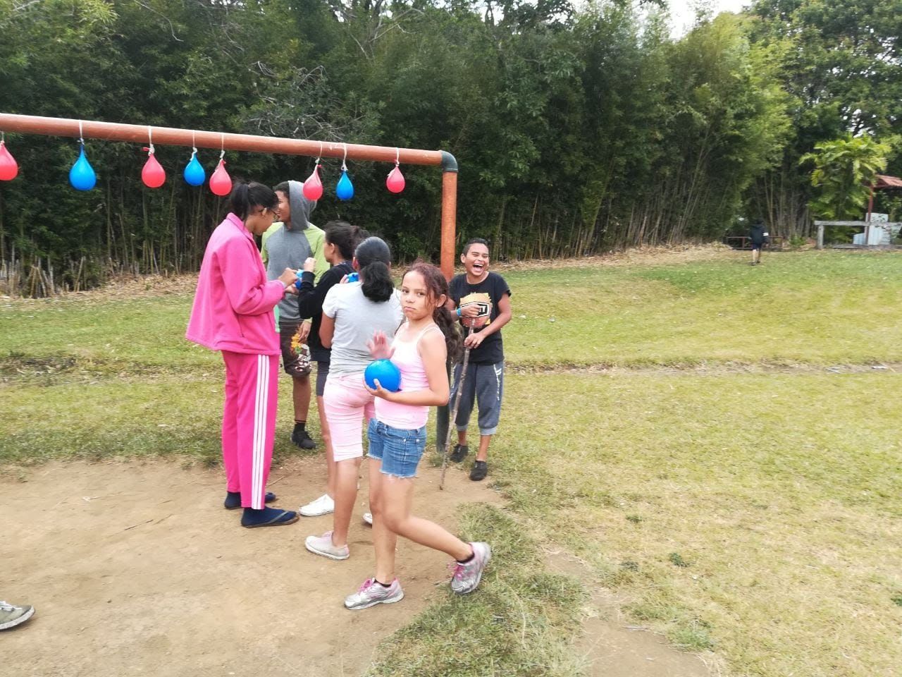 Participantes jugando al aire libre, con globos de agua colgados de una estructura de metal